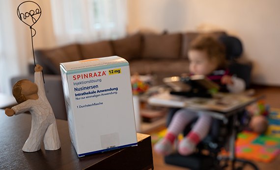Упаковка препарата "Спинраза" на фоне комнаты с маленьким ребенком