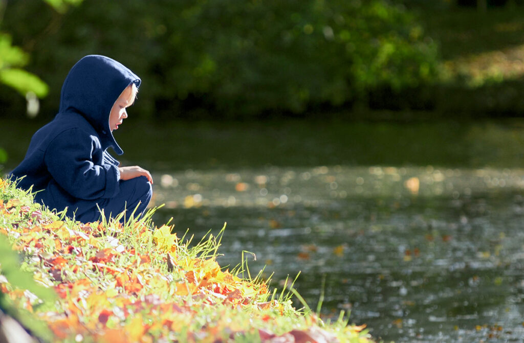 Ребенок сидит на берегу пруда в Центральном парке культуры и отдыха