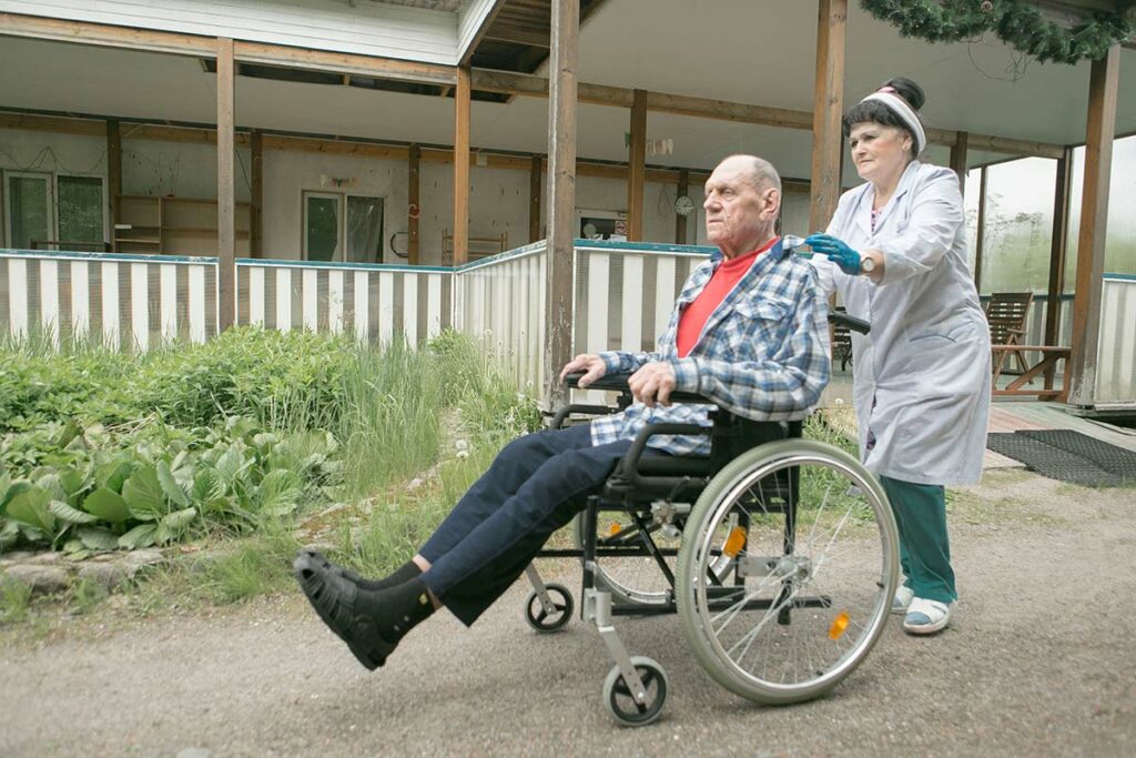 Медсестра везет на инвалидной коляске Евгения Николаевича 