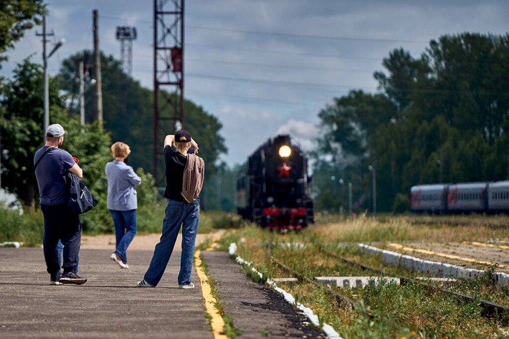 Старинный поезд прибывает на станцию, пассажиры фотографируют