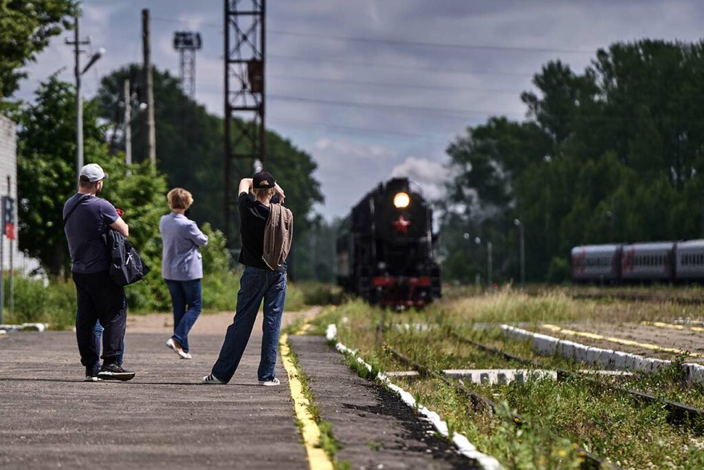 Старинный поезд прибывает на станцию, пассажиры фотографируют