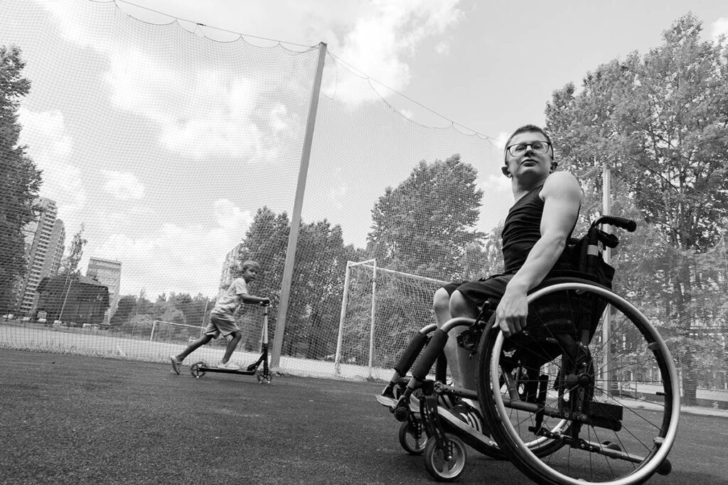Черно-белая фотография. Миша Канашев на коляске на спортивной площадке