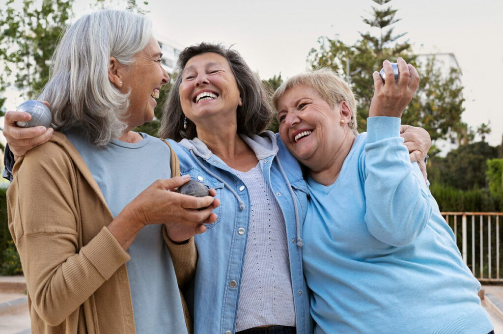 Женщины-подруги старшего возраста весело смеются и играют в петанг