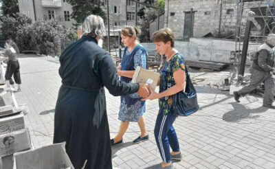 Священник передает двум женщинам гуманитарную помощь