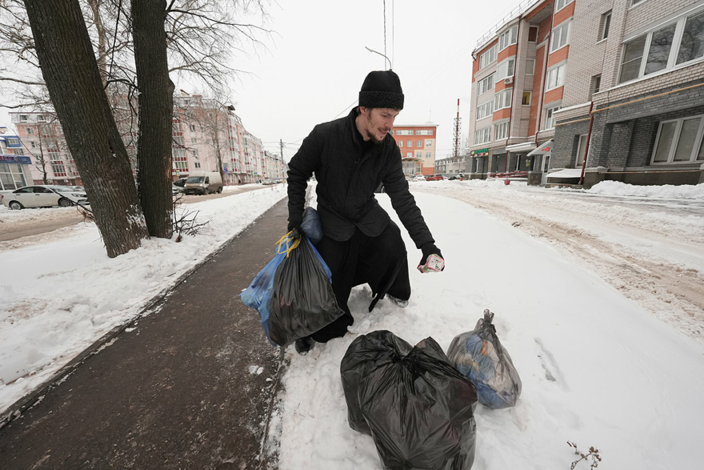 отец Александр убирает мусор на улице города 